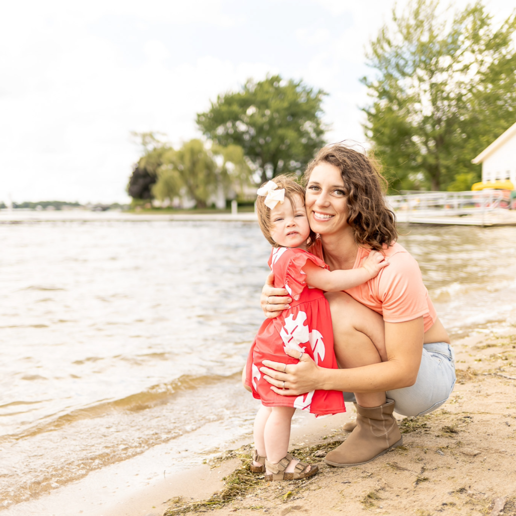 mother and daughter crouch at shore of a lake on a cloudy day